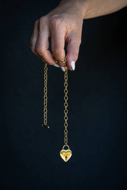 The hand holds a chain with a heart-shaped locket.